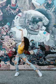 Woman dancing in front of a vibrant graffiti wall featuring an astronaut. Curly hair and ripped jeans enhance the street style.