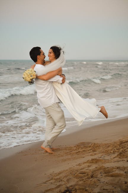 Joyful couple in wedding attire celebrating love on a serene beach.